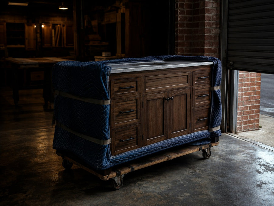 A solid wood vanity wrapped in moving blankets on a dolly at the cabinet shop door
